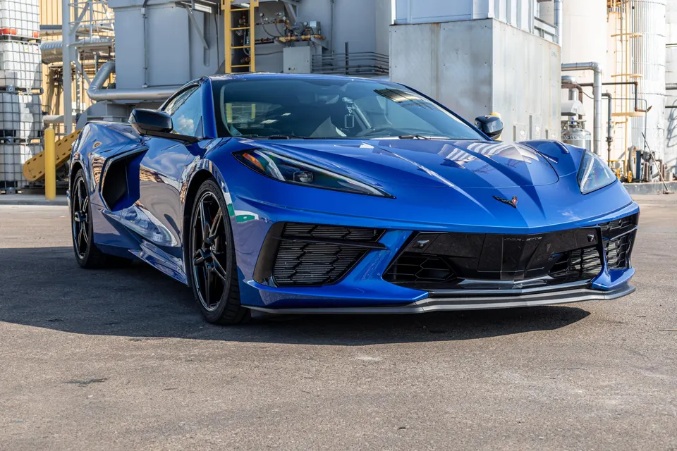 Blue Chevrolet Corvette C8 sports car parked in an industrial setting, showcasing its sleek front design.