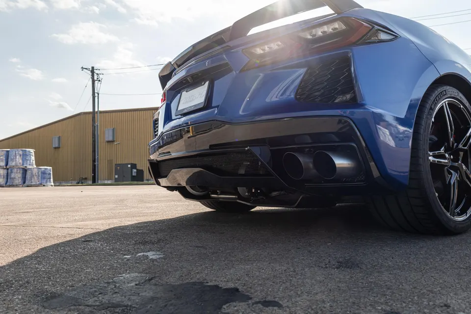 A blue C8 Corvette with an aftermarket exhaust system and rear diffuser, parked outdoors.