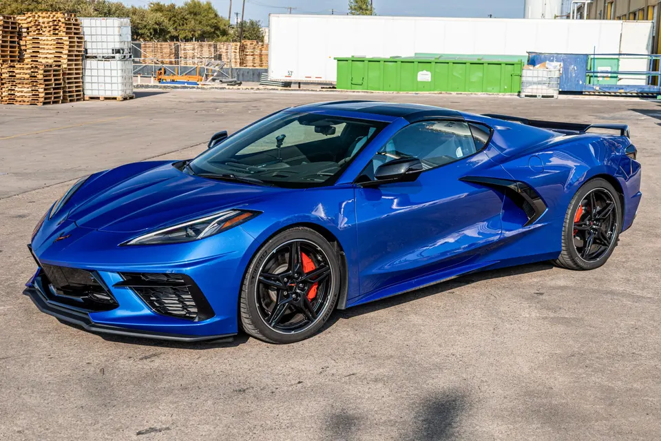 Blue Chevrolet Corvette C8 with black aftermarket wheels and red brake calipers parked in a lot.