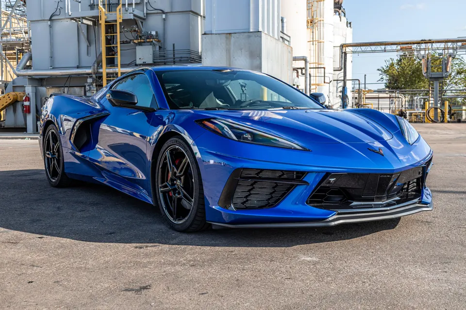 Blue Chevrolet Corvette C8 parked outdoors with an industrial building in the background, showcasing its sleek design.