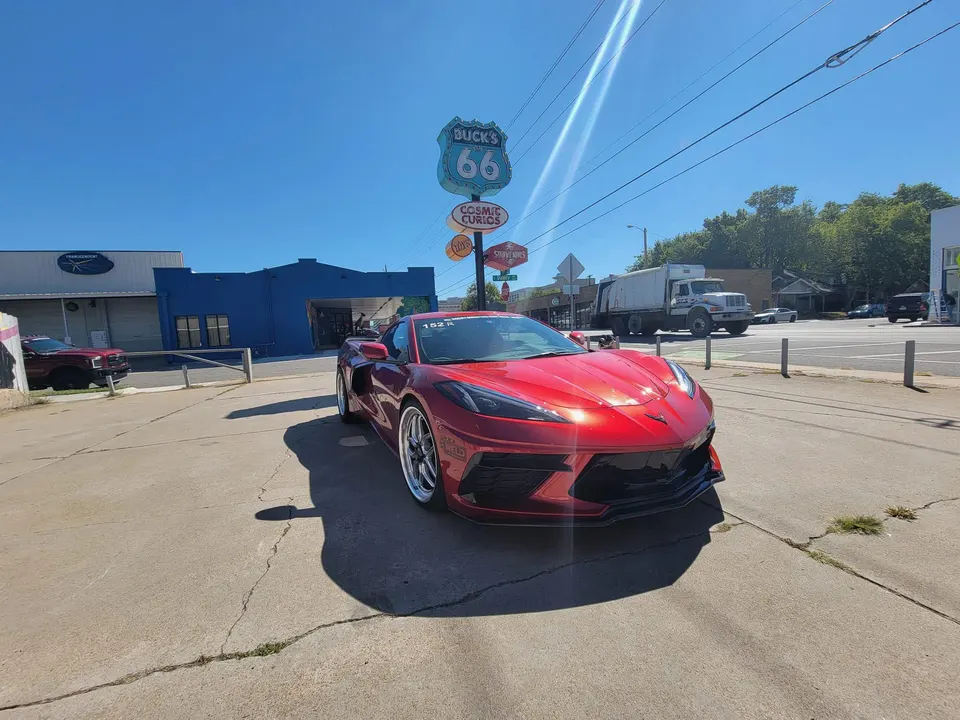 Red Chevrolet Corvette C8 parked on a sunny street in front of a "Buck's 66" sign and blue building.