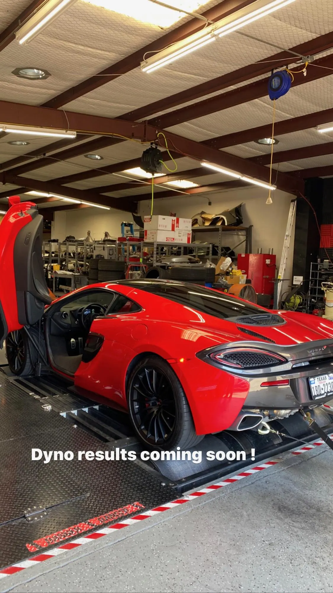 A red McLaren supercar on a dynamometer at a performance tuning shop, with its doors open, ready for power testing.