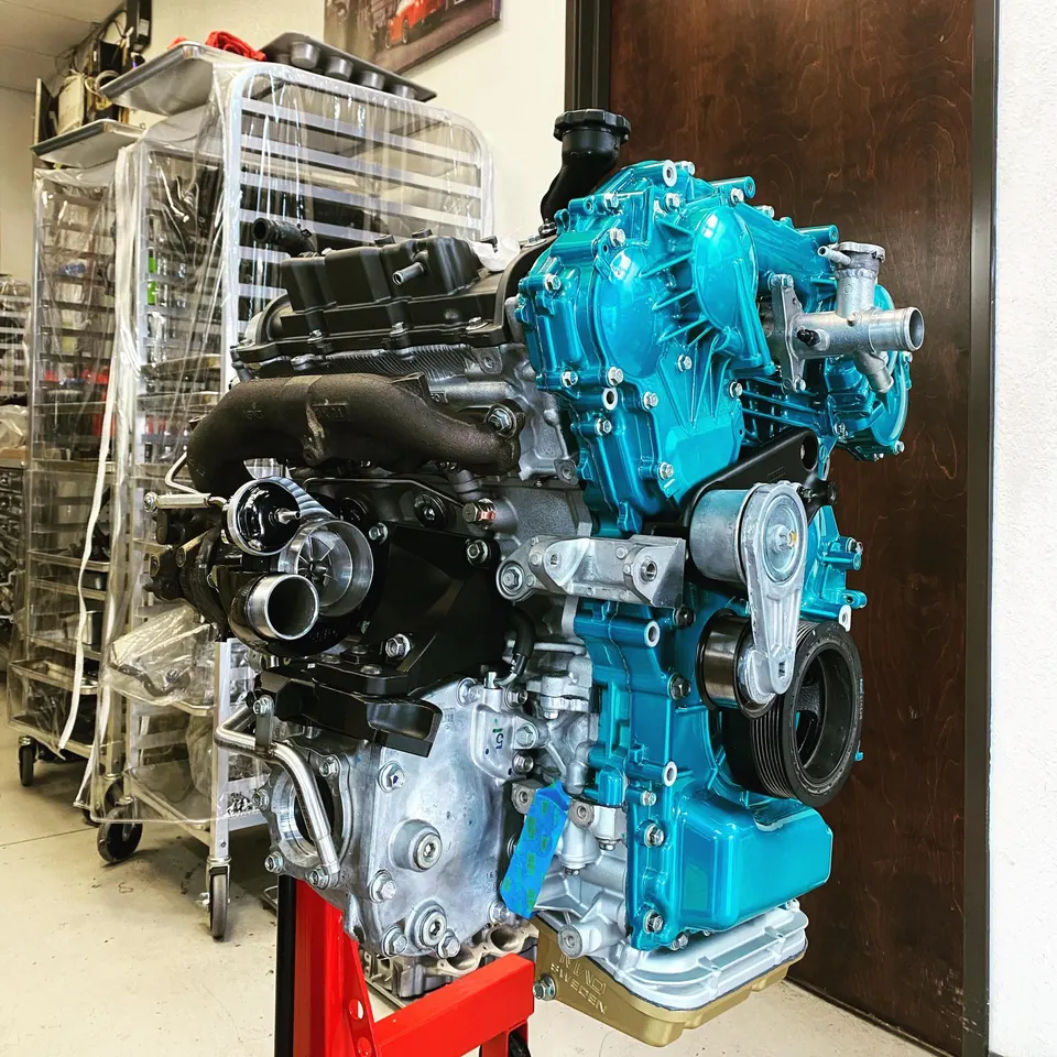 A built engine with a vibrant blue intake manifold and a turbocharger, displayed on an engine stand in a performance shop.