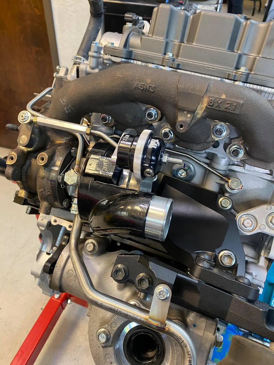 Close-up of a performance engine build in a shop, featuring a turbocharger, wastegate, and exhaust manifold.