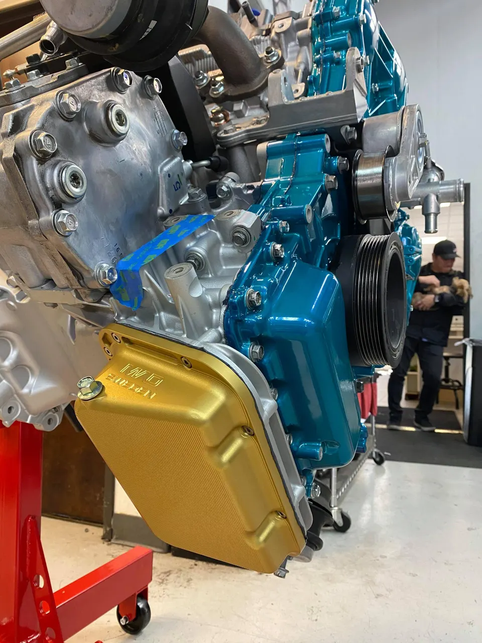 A detailed view of a custom-built engine with a gold oil pan and blue engine block on a stand in a workshop.