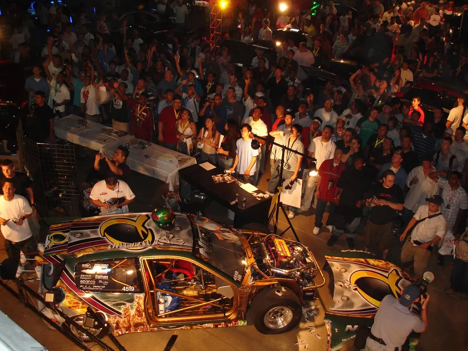 Highly modified drag race car on display at a car show, surrounded by a large crowd of spectators.