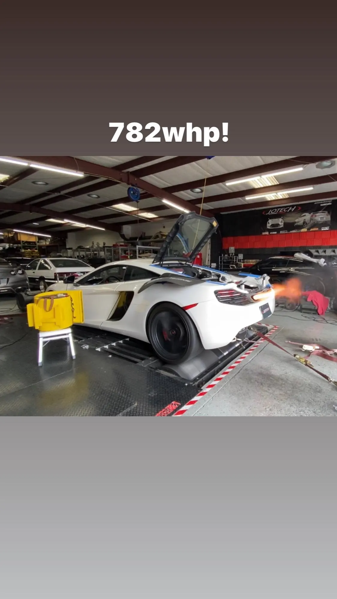 A white McLaren supercar on a dyno at Jotech Motorsports, producing 782 wheel horsepower with exhaust flames.