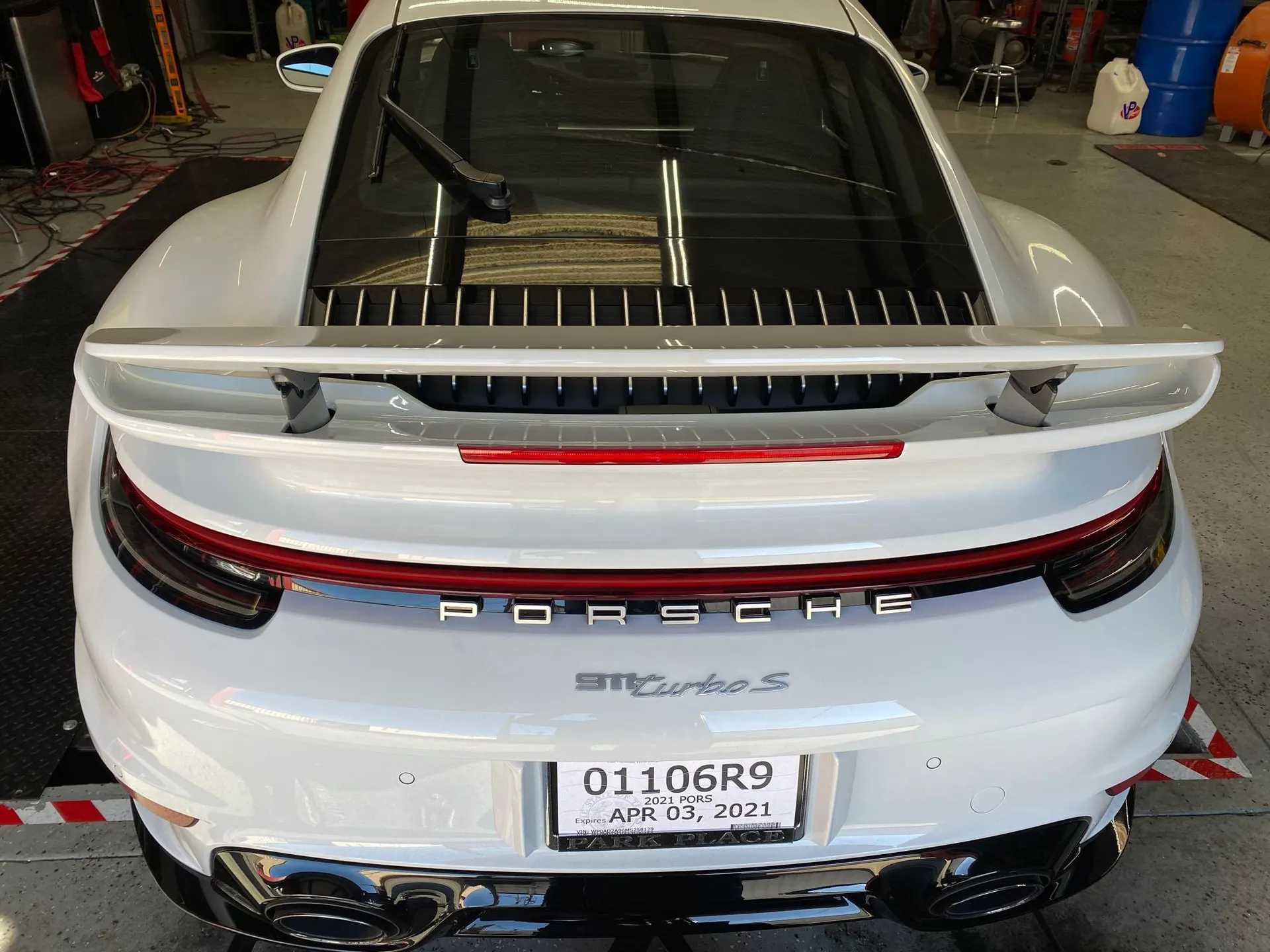 Rear view of a white Porsche 911 Turbo S in a shop, showcasing its rear wing and exhaust tips.