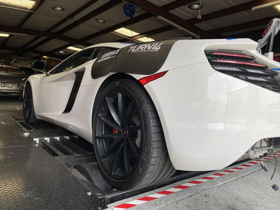 White McLaren supercar on a dyno at a performance tuning shop, ready for performance testing and tuning.
