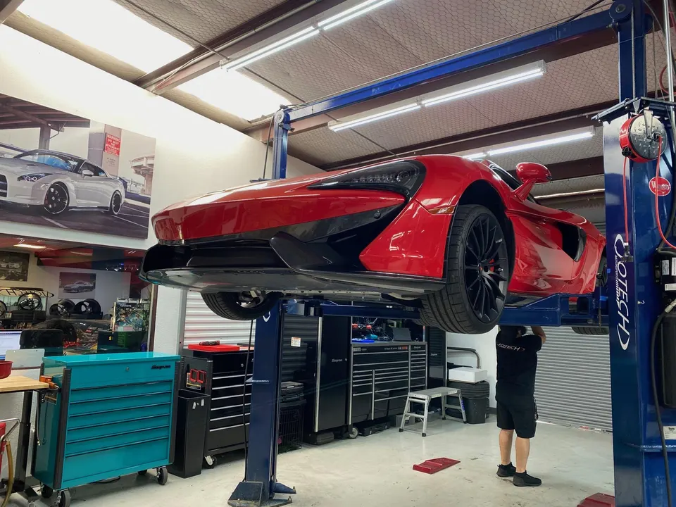 Red McLaren supercar on a hydraulic lift in a performance tuning shop with a mechanic working underneath.