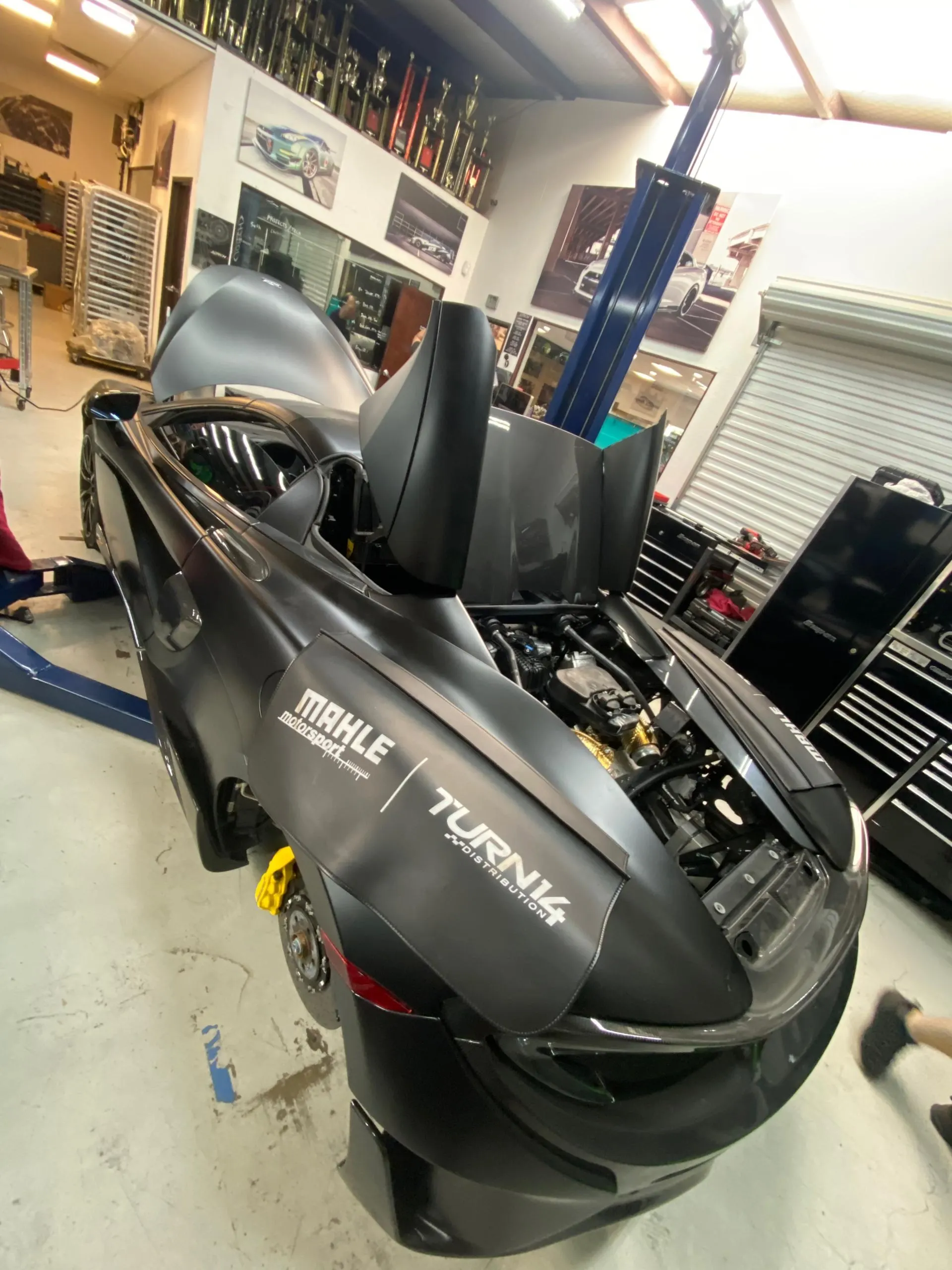 McLaren supercar on a lift in a performance tuning shop with its engine bay open for service or modification.