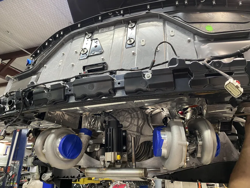 Underside view of a performance car on a lift, showcasing twin turbochargers being installed in a shop.