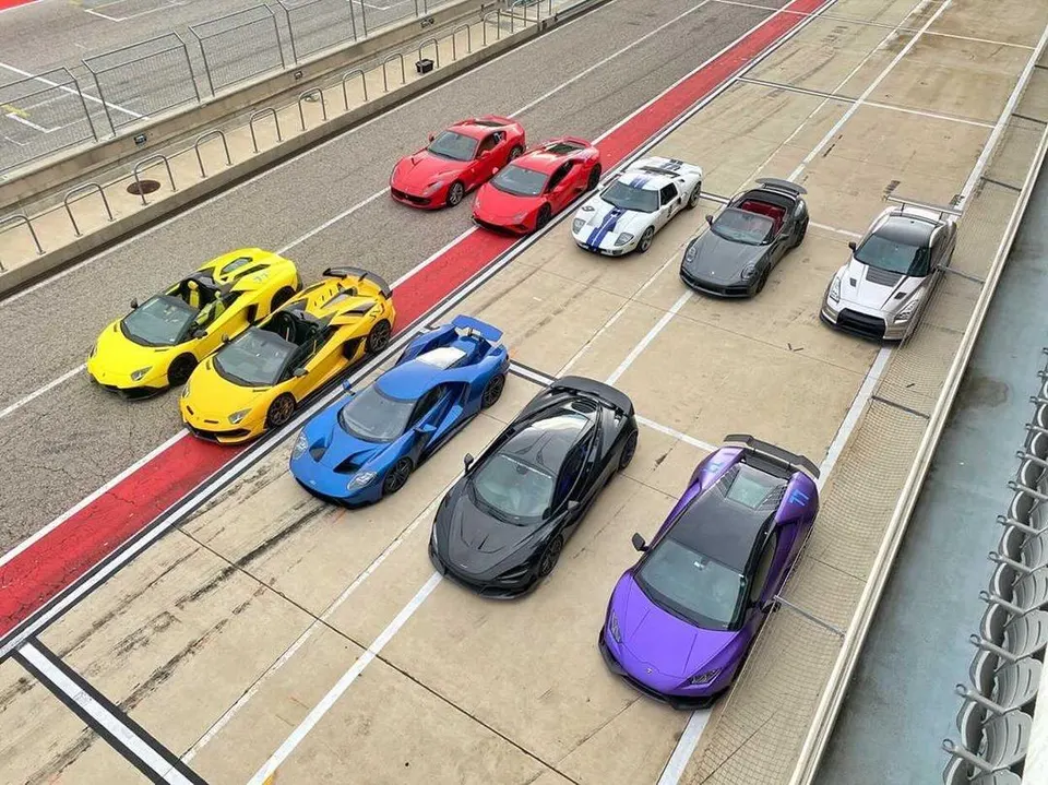 A high-angle shot of multiple supercars including Lamborghinis, Ford GT, McLaren, Porsche, Nissan GT-R, and Ferraris lined up on a track.