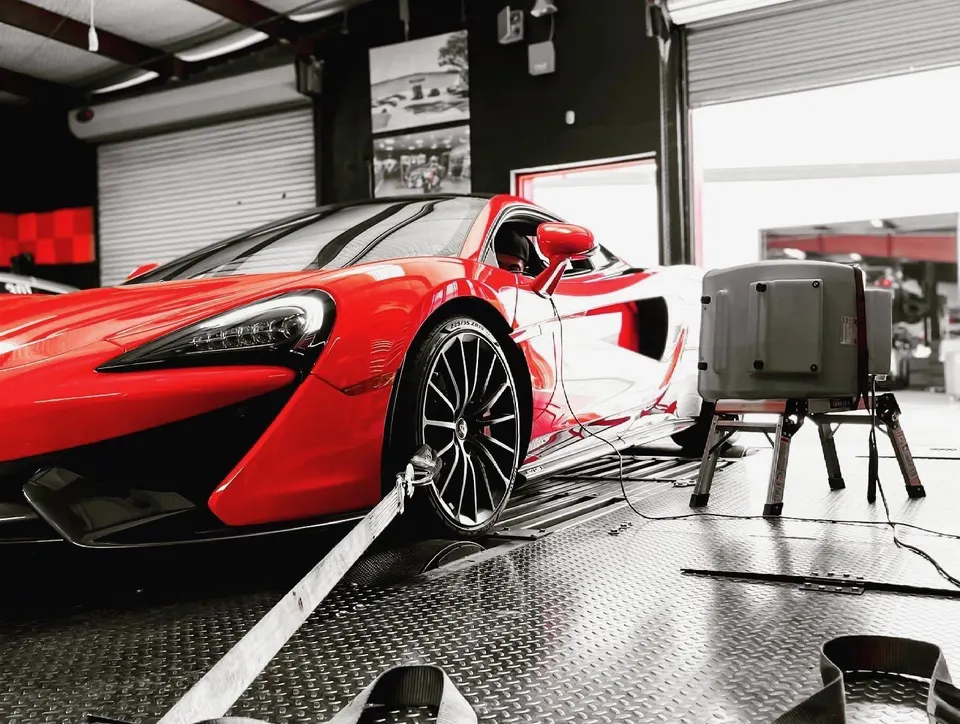 Red McLaren supercar strapped to a dynamometer in a performance tuning shop, undergoing a power test.