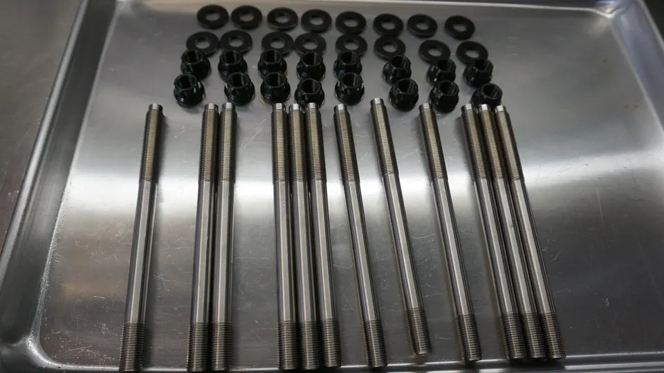 High-performance engine studs, nuts, and washers laid out on a metal tray, ready for engine assembly.