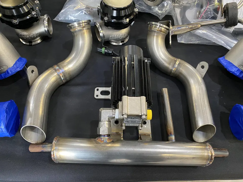 High-performance turbo system components including Precision Turbo wastegates and stainless steel piping laid out in a shop.