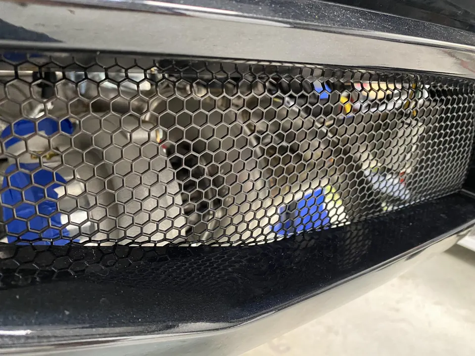 A close-up view of a car's front bumper grille with a honeycomb mesh pattern, revealing an intercooler behind it.