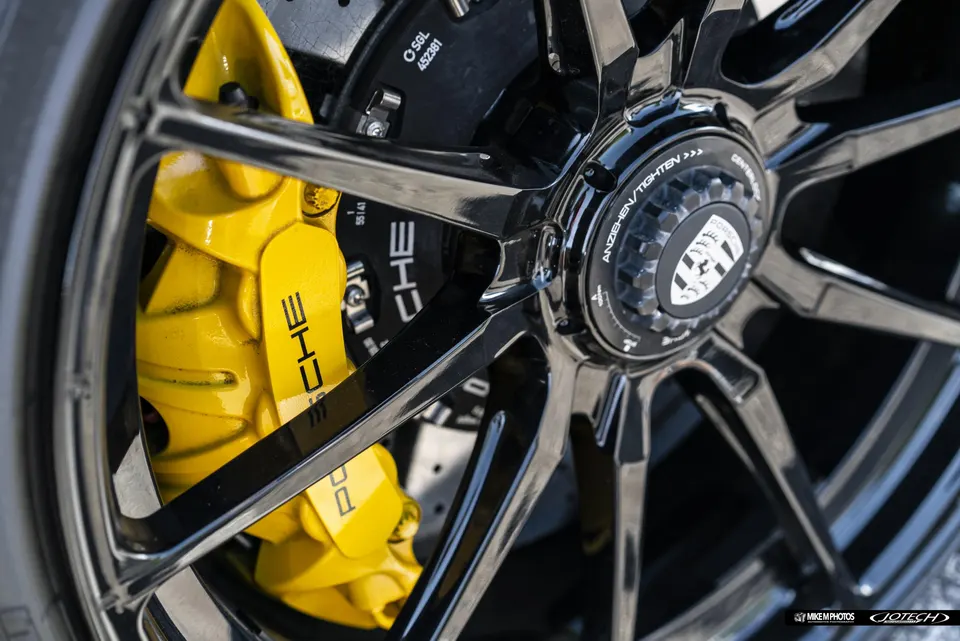 Close-up of a black Porsche centerlock wheel with bright yellow brake calipers and a drilled rotor.
