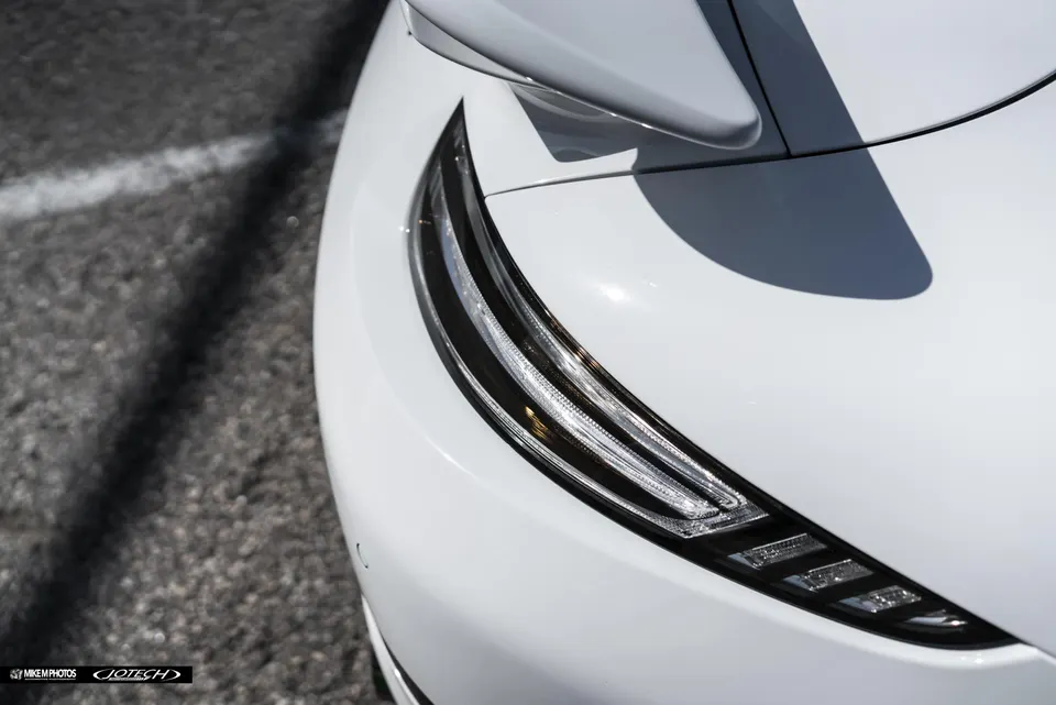 Close-up of a white car's modern LED headlight and front fender in bright sunlight.