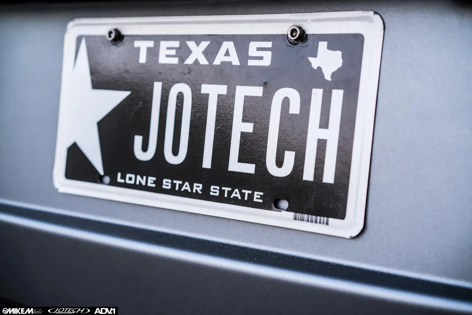 Close-up of a custom Texas license plate reading JOTECH, mounted on a vehicle.