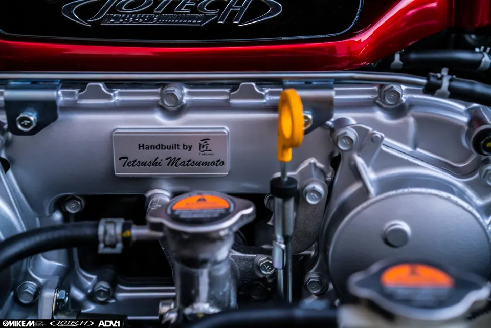 Close-up of a Jotech built engine, featuring a 'Handbuilt by Tetsushi Matsumoto' plaque and red engine cover.