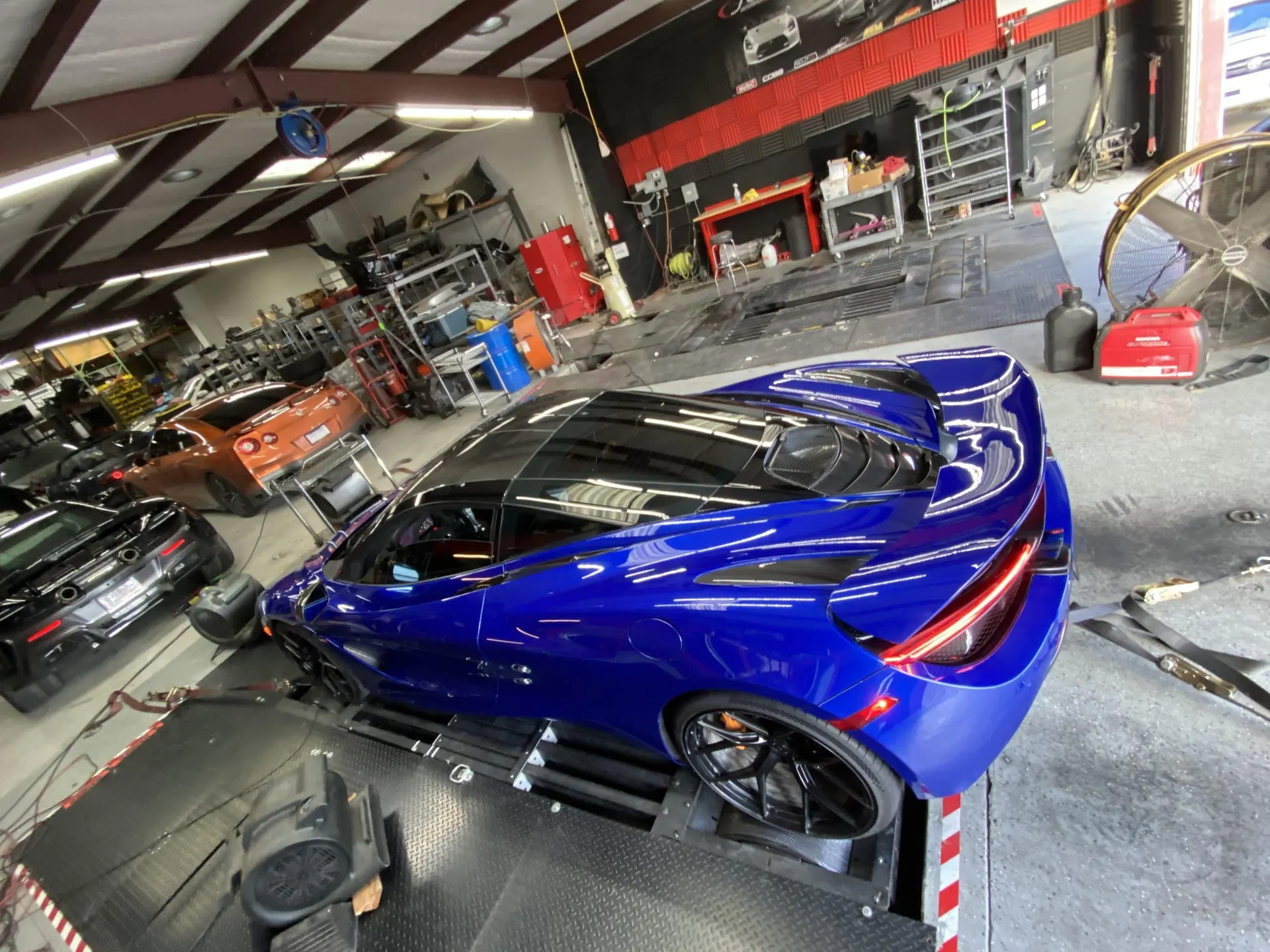 Blue McLaren 720S strapped to a dynamometer for performance tuning at a shop.
