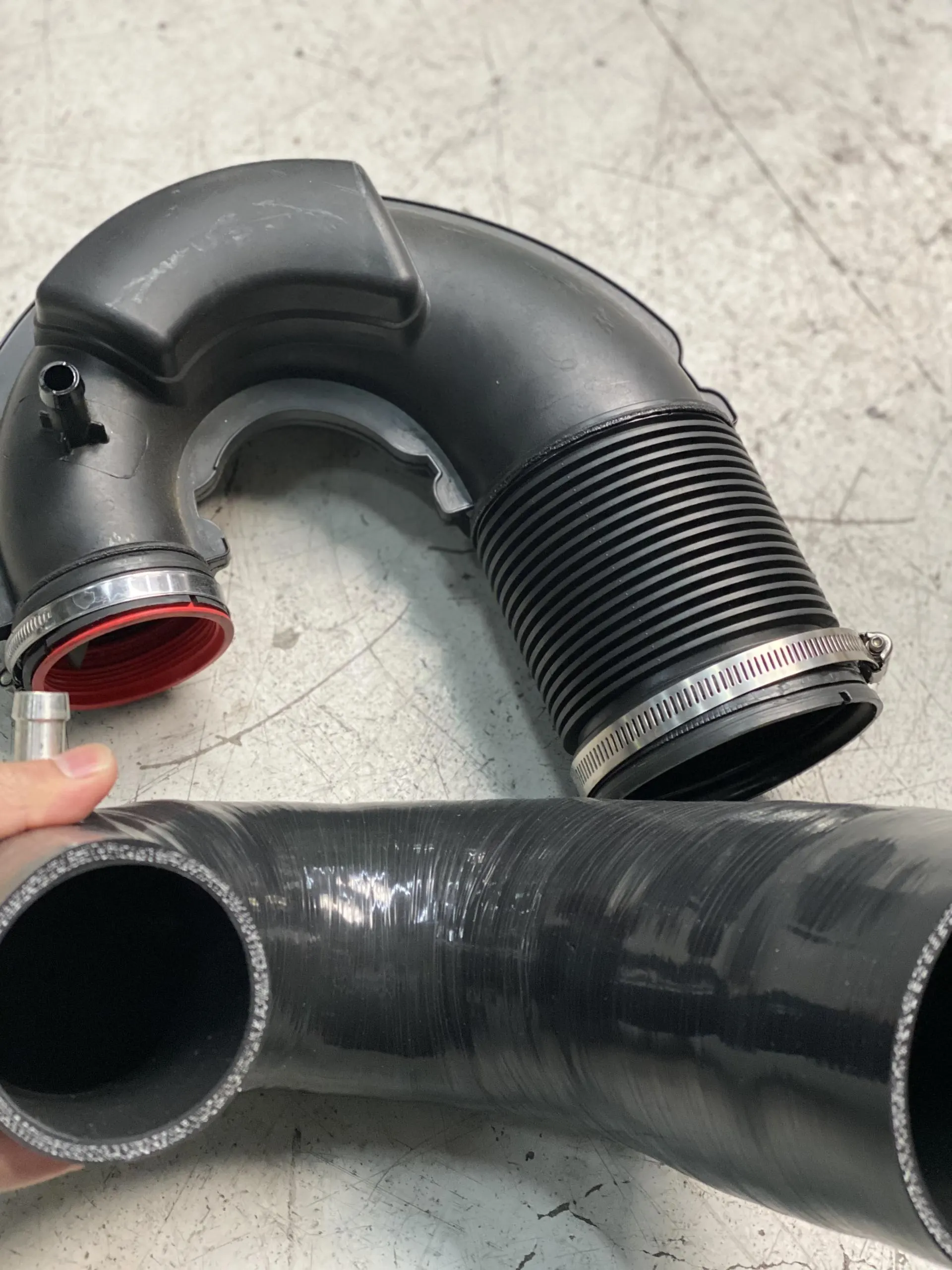Black plastic and silicone intake pipes for a performance car on a shop floor, ready for installation.