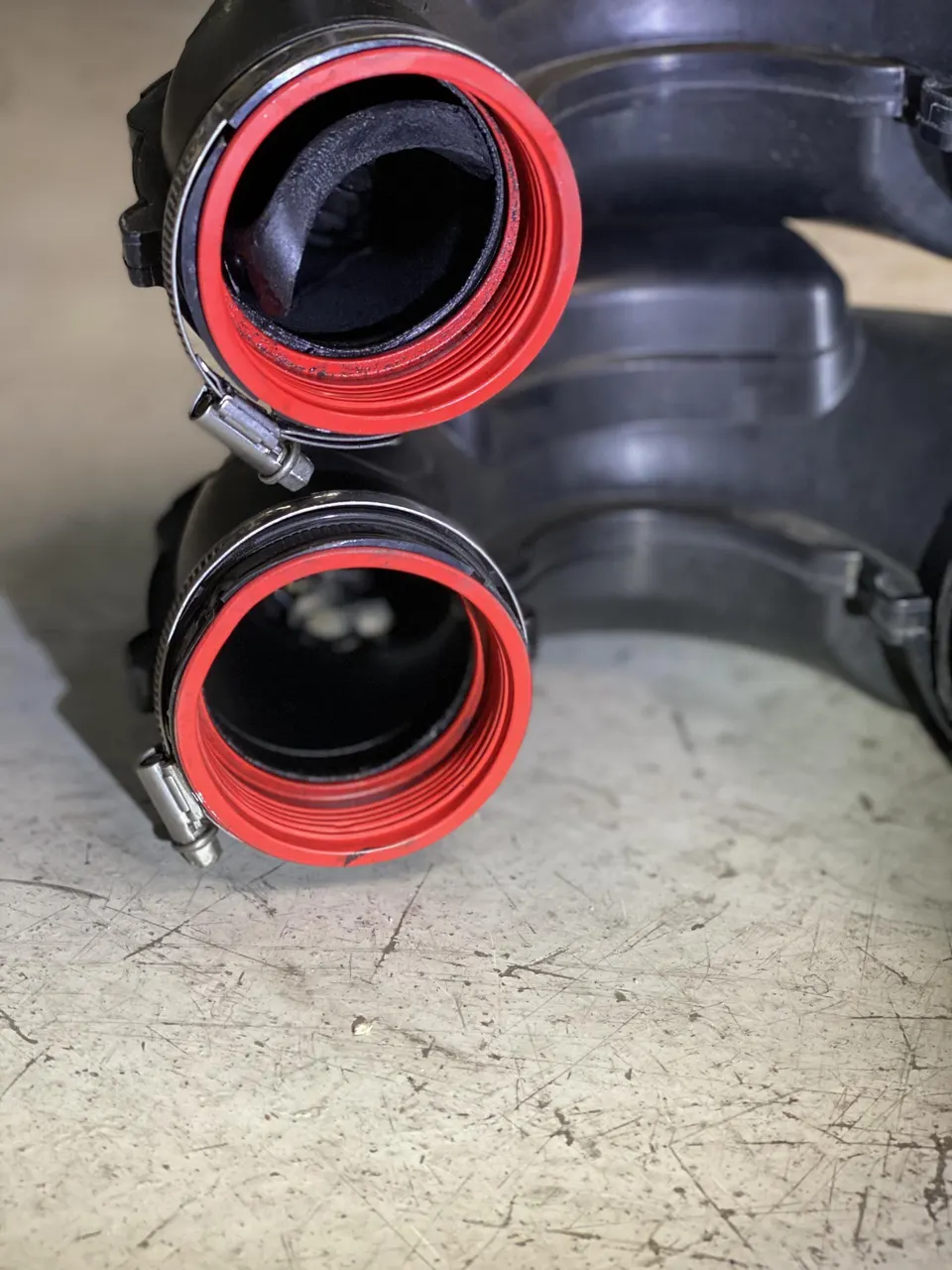 Close-up of black induction pipes with red silicone couplers and metal clamps on a shop floor.