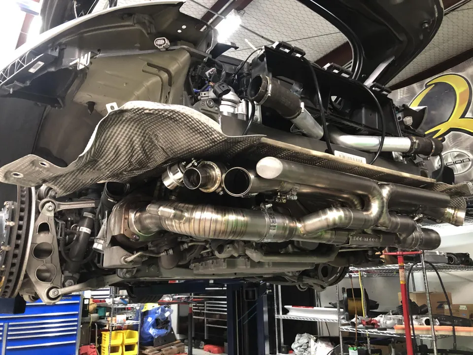 A McLaren on a lift in a shop, showcasing a custom titanium exhaust system and carbon fiber heat shield installation.