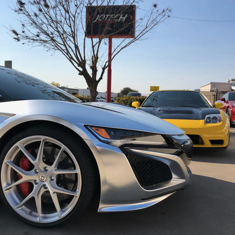 Silver Acura NSX and yellow Honda NSX parked outside Jotech Motorsports facility, showcasing custom wheels and brakes.