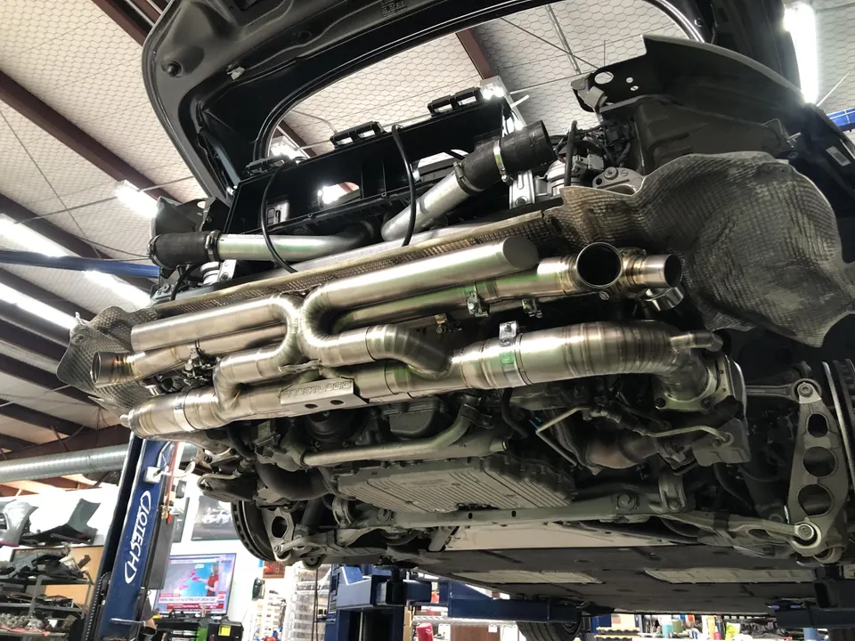 Underside view of a performance car on a lift, showcasing a custom aftermarket exhaust system installation in a shop.