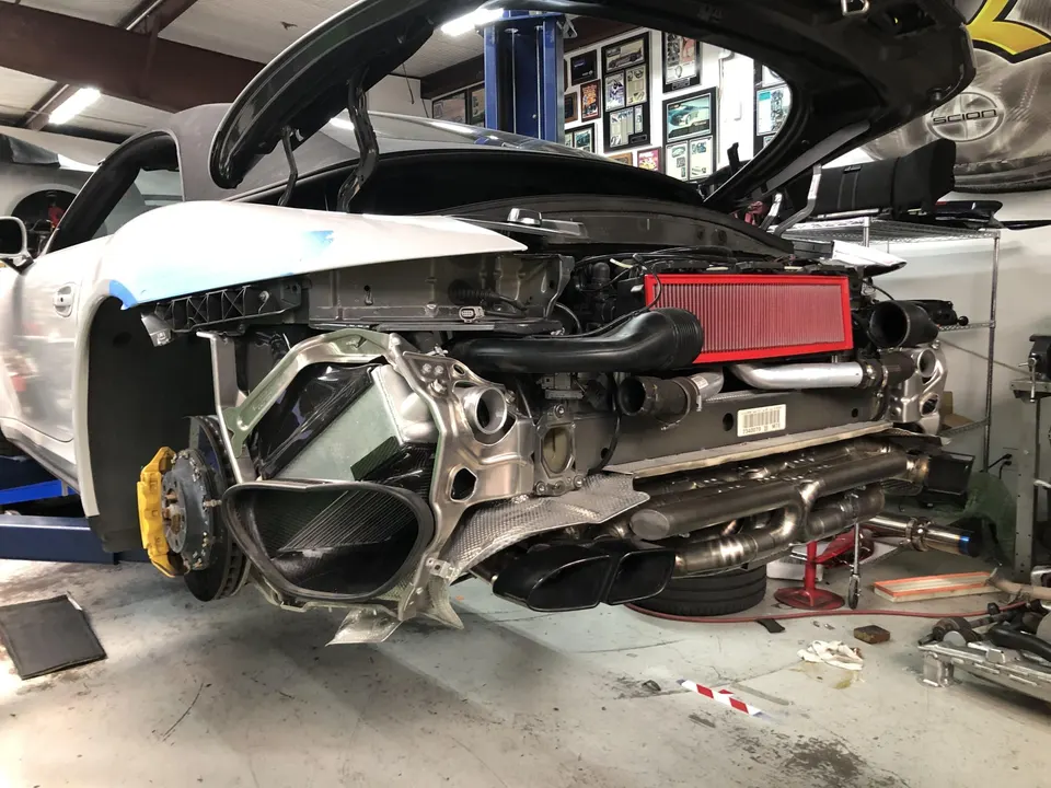 Porsche 911 undergoing performance exhaust and induction system installation in a tuning shop.