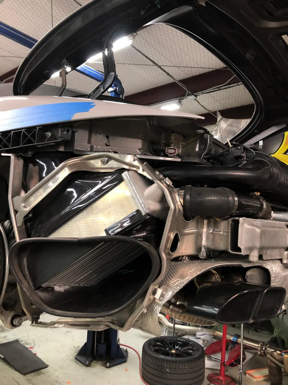 Rear view of a McLaren supercar on a lift in a performance shop, showcasing carbon fiber intake and exhaust system.