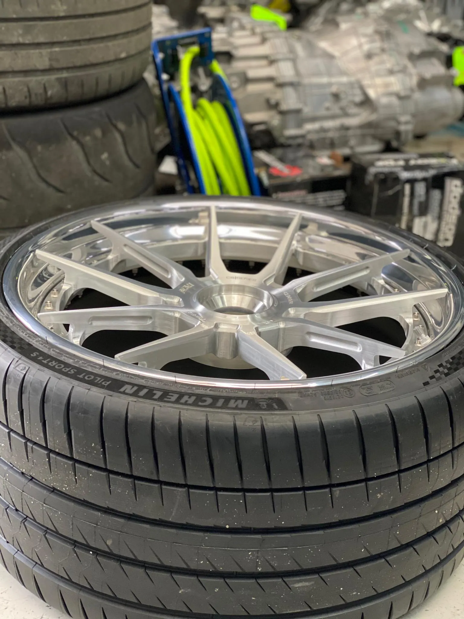 Close-up of a custom silver multi-spoke wheel mounted with a Michelin Pilot Sport 4S tire in a shop setting.