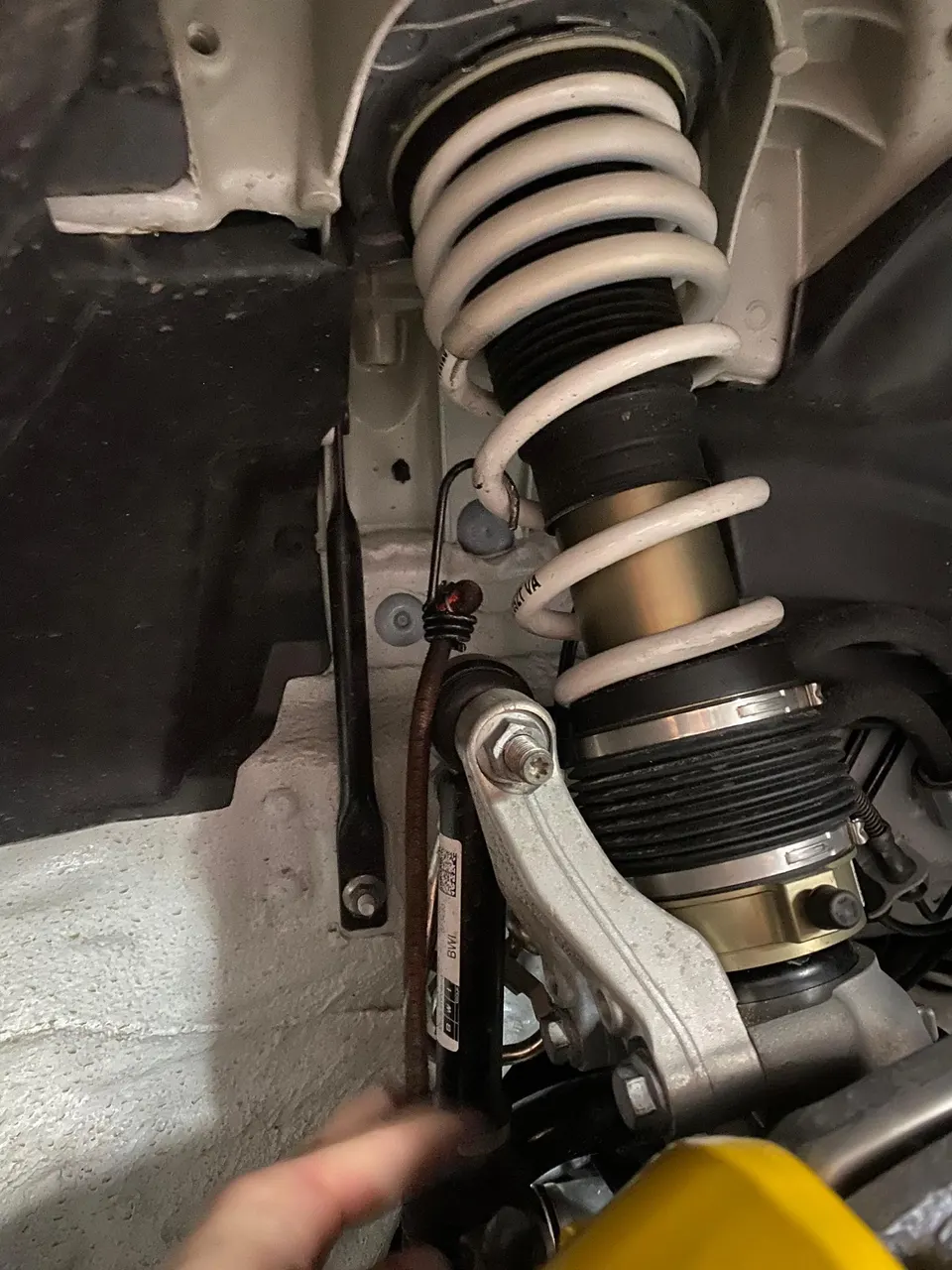 A close-up view of a car's suspension system, showing a white coilover spring and shock absorber assembly.