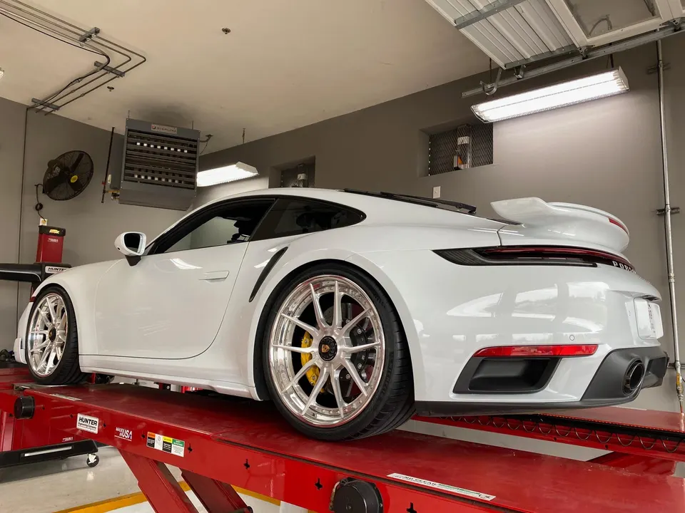 White Porsche 911 on a red shop lift, showcasing custom multi-spoke wheels with yellow brake calipers.