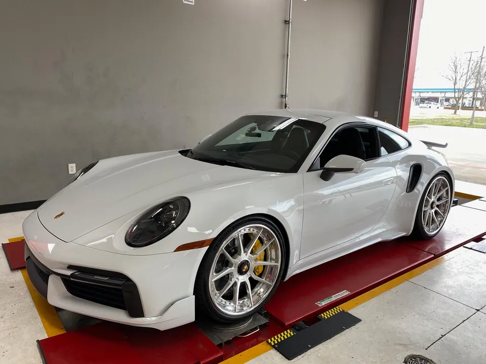 White Porsche 911 Turbo S on a dyno at a performance tuning shop, showcasing aftermarket wheels and yellow brake calipers.