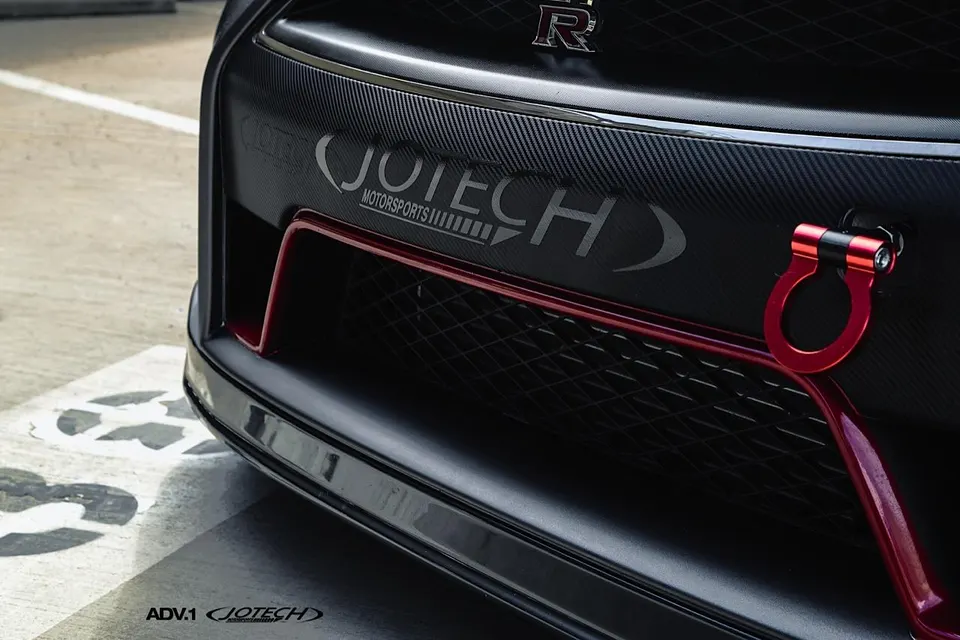 Close-up of a Nissan GT-R's carbon fiber front bumper with a red tow hook and Jotech Motorsports branding.