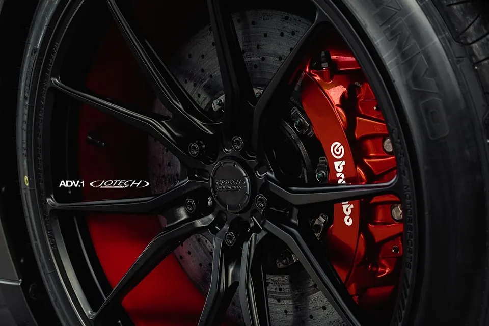 Close-up of a black ADV.1 wheel with red Brembo brake calipers and a performance tire, featuring Jotech Motorsports branding.