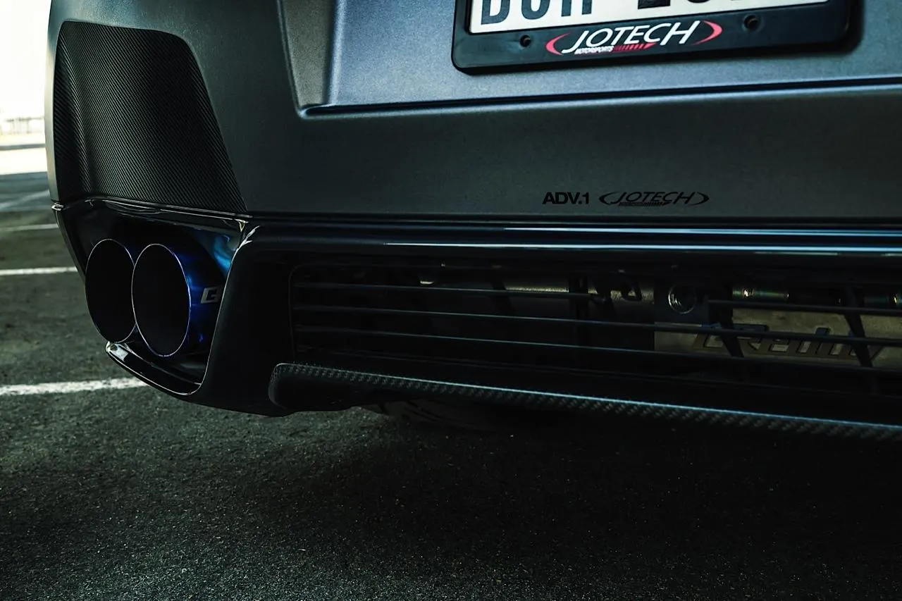 A close-up of a matte grey car's rear bumper with blue titanium exhaust tips and a carbon fiber diffuser.