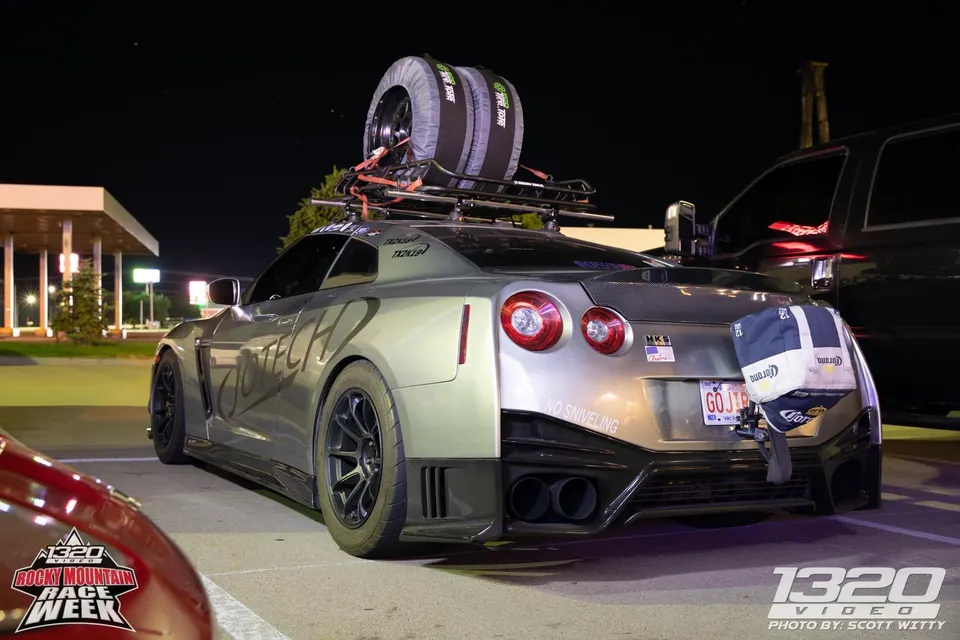 Silver Nissan GT-R with Jotech branding, a roof rack carrying spare tires, and aftermarket exhaust, parked at night during Rocky Mountain Race Week.