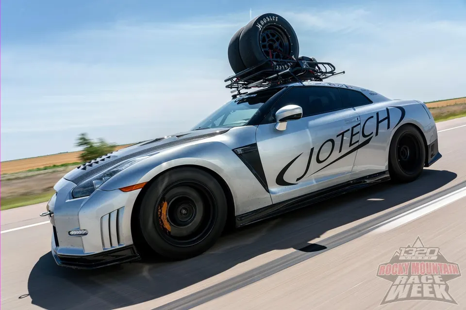 Silver Jotech Nissan GT-R with drag wheels and a roof rack carrying Hoosier tires on a highway.