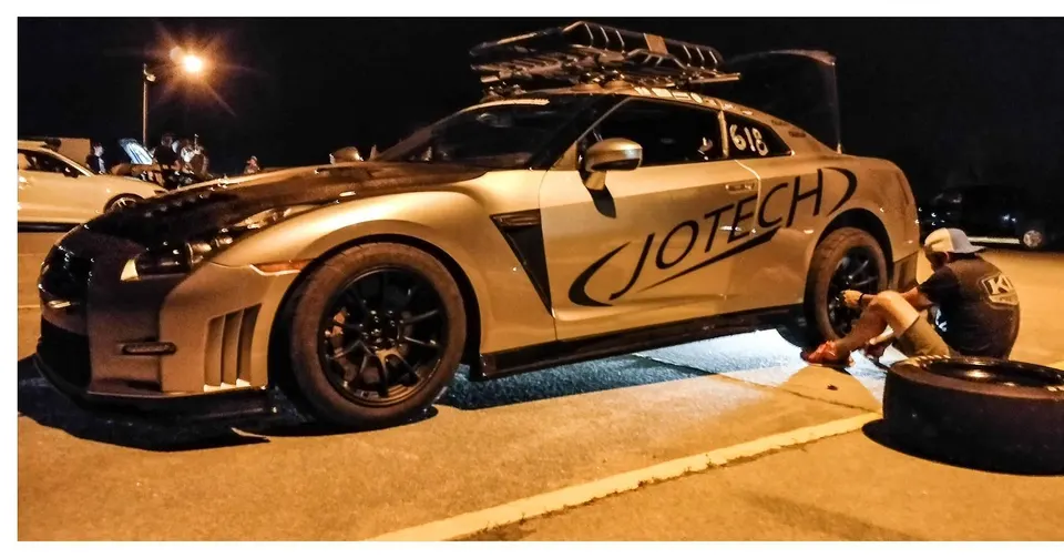 Jotech Nissan GT-R #618 at night, with a crew member changing a rear wheel at the track.