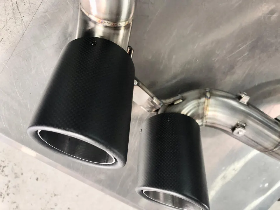Close-up of carbon fiber exhaust tips and stainless steel piping on a performance car, showcasing the detail and craftsmanship.