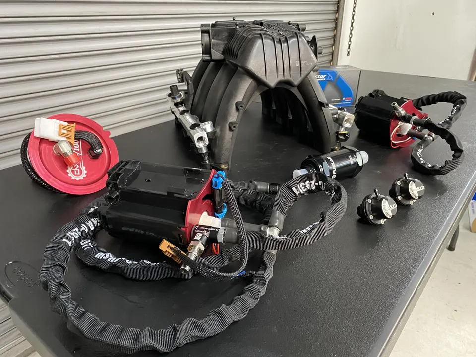 Aftermarket performance parts including an intake manifold, fuel pumps, and fuel rails laid out on a table.