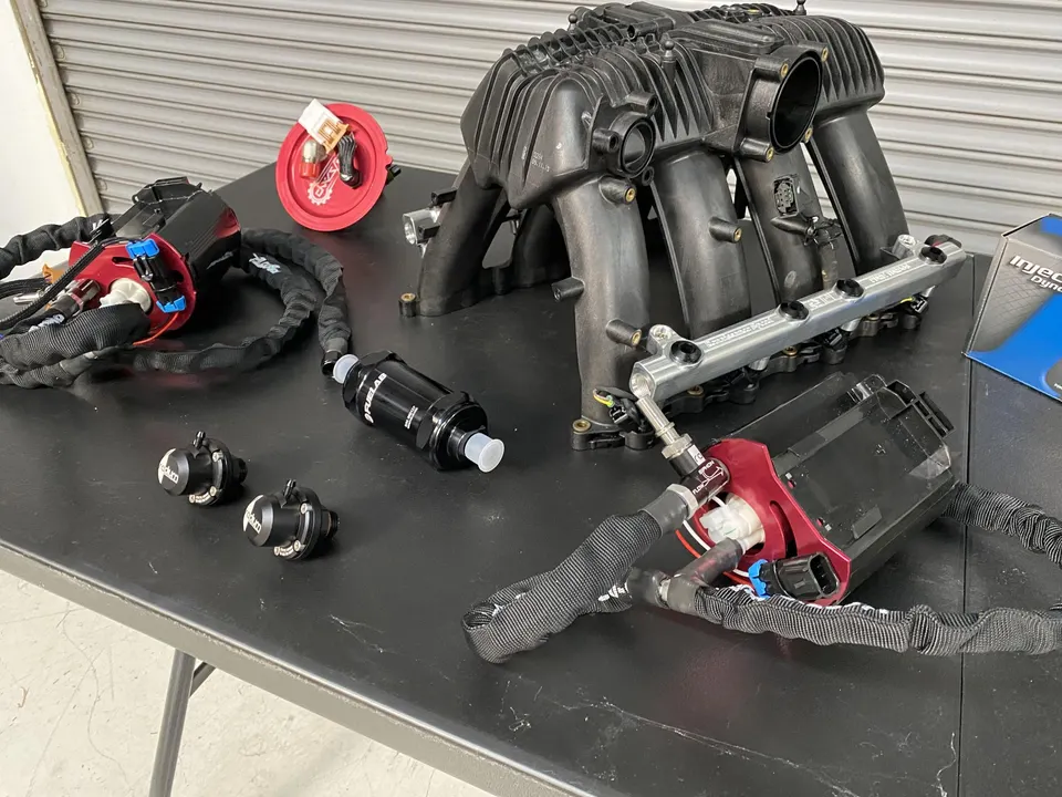 Performance fuel system components including fuel pumps, fuel filter, fuel rail, and an intake manifold on a table.