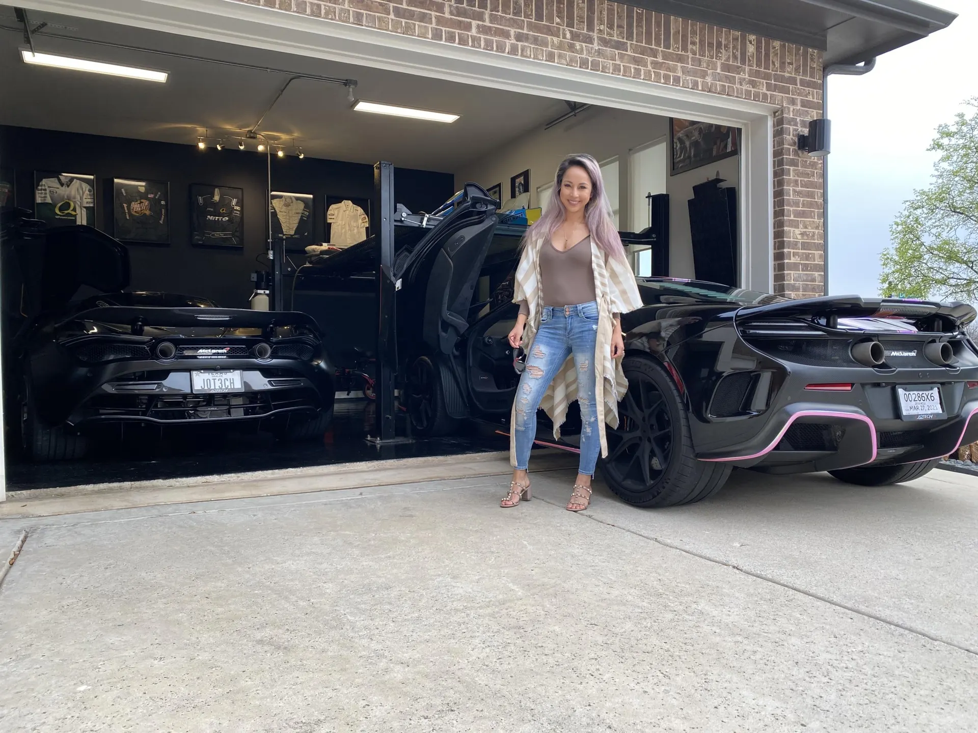 A woman stands between two black McLarens in a well-lit garage, showcasing the high-performance supercars.