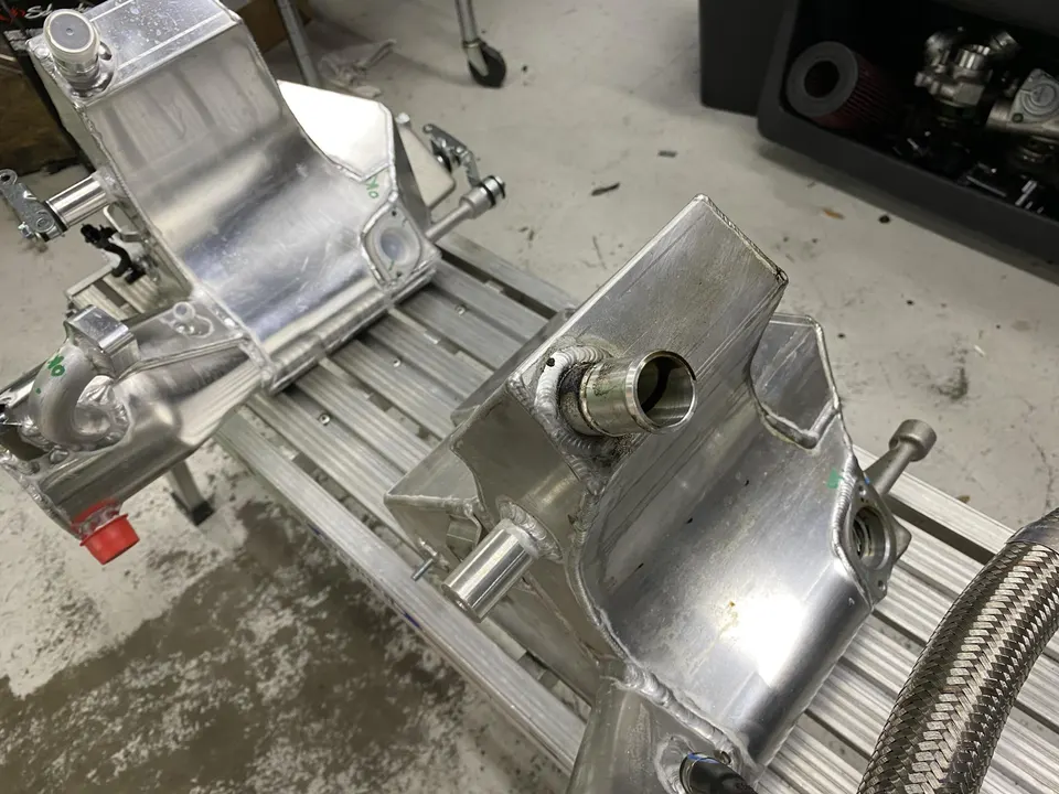 Custom aluminum intercoolers with welded fittings on a metal rack in a performance shop.