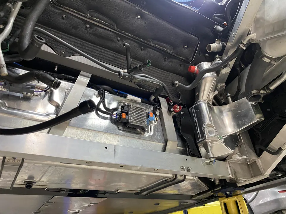 Underside view of a performance car on a lift, showing intercooler, hoses, and wiring.