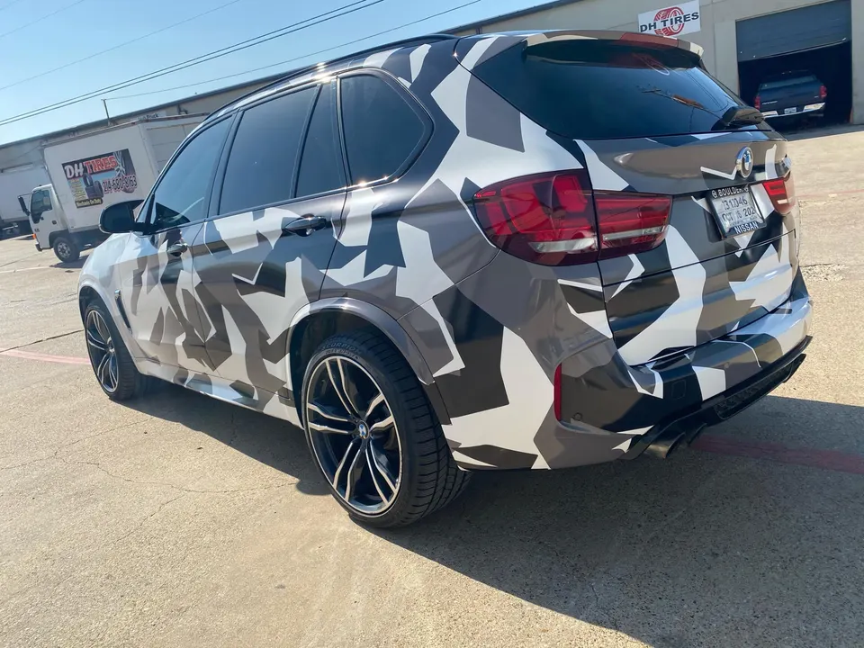 BMW X5 SUV with a unique camouflage wrap and aftermarket wheels parked outside a shop.